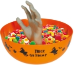 Oranžová halloweenská miska s vyčnívající šedou rukou, naplněná sladkostmi